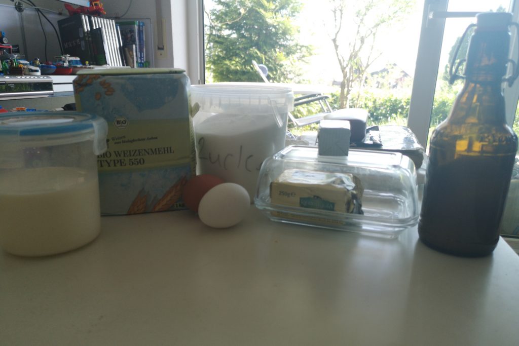 Im Bild zu sehen die Zutaten für die Buns, von lienks nach Rechts, Milch, Weizenmehl Typ 550, Eier, Zucker, Butter, Hefe und Salz in einer Bögelbuddel
